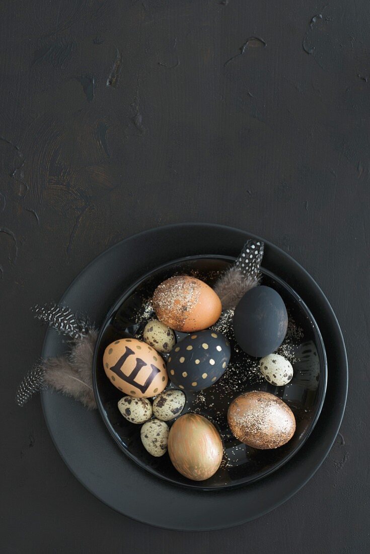 Black and gold Easter eggs, feathers and quail eggs in black bowl
