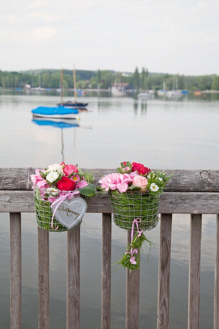 Two metal baskets filled with grass and flowers on balustrade next to lake