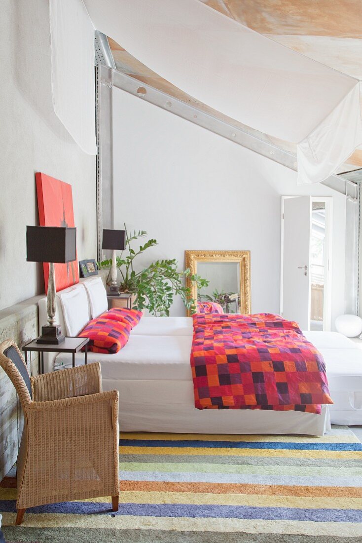 Helles Dachgeschossschlafzimmer mit farbenfroher Bettwäsche, abgehängter weißer Stoffbahn und Streifenteppich