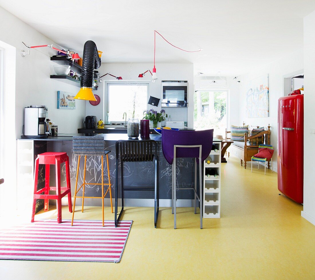 Verschiedene Barhocker in bunter, offener Küche mit gelbem Boden