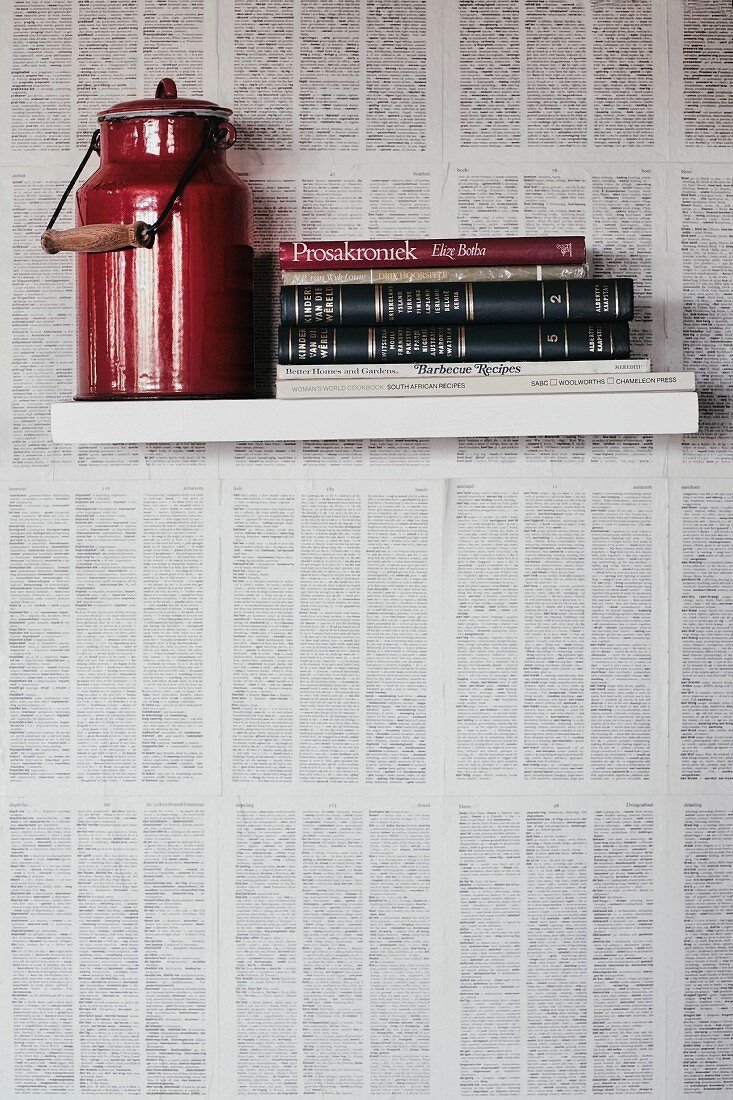 Wandbord mit roter Milchkanne und Büchern auf mit Papier tapezierter Wand