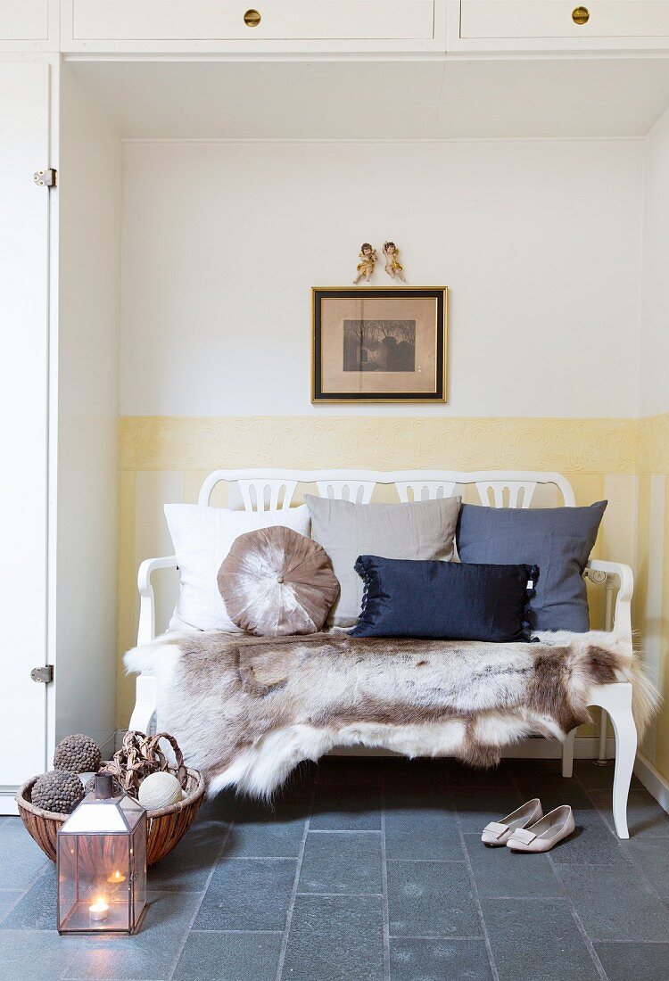 Fur rug and scatter cushions on wooden couch in niche surrounded by fitted cupboards