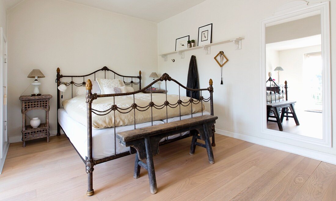 Rustic wooden bench at foot of old metal bed in bedroom