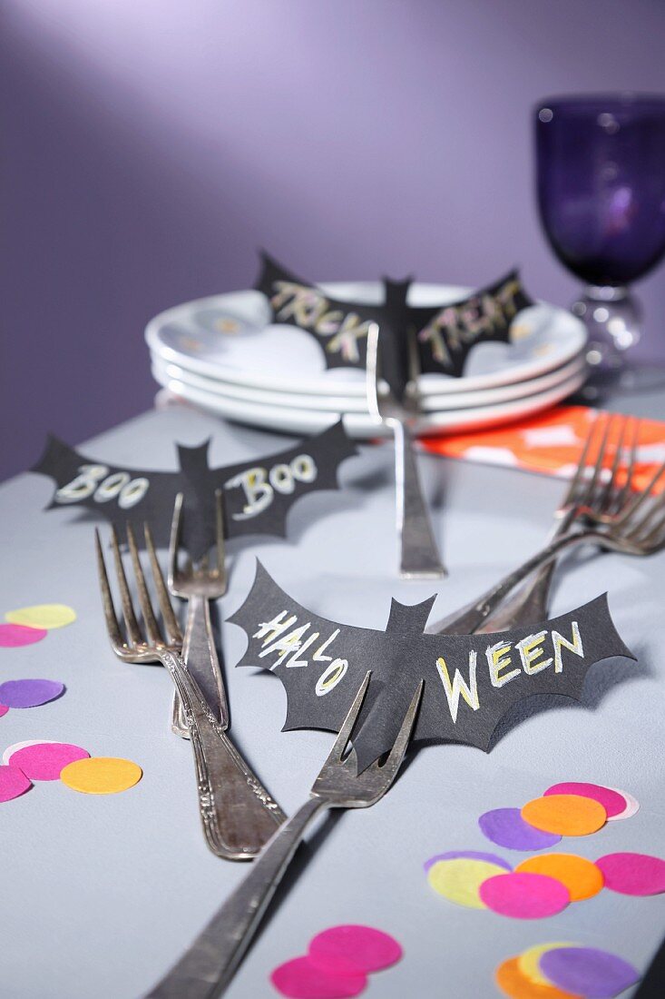 Halloween-Tischdekoration mit ausgeschnittenen und beschrifteten Fledermausmotiven auf Gabeln gesteckt