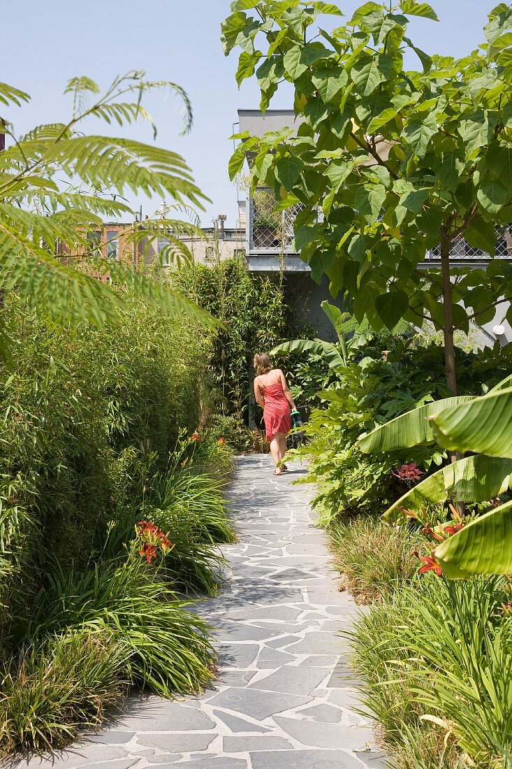 Sommerlicher Garten mit Natursteinplattenweg und Frau im Hintergrund