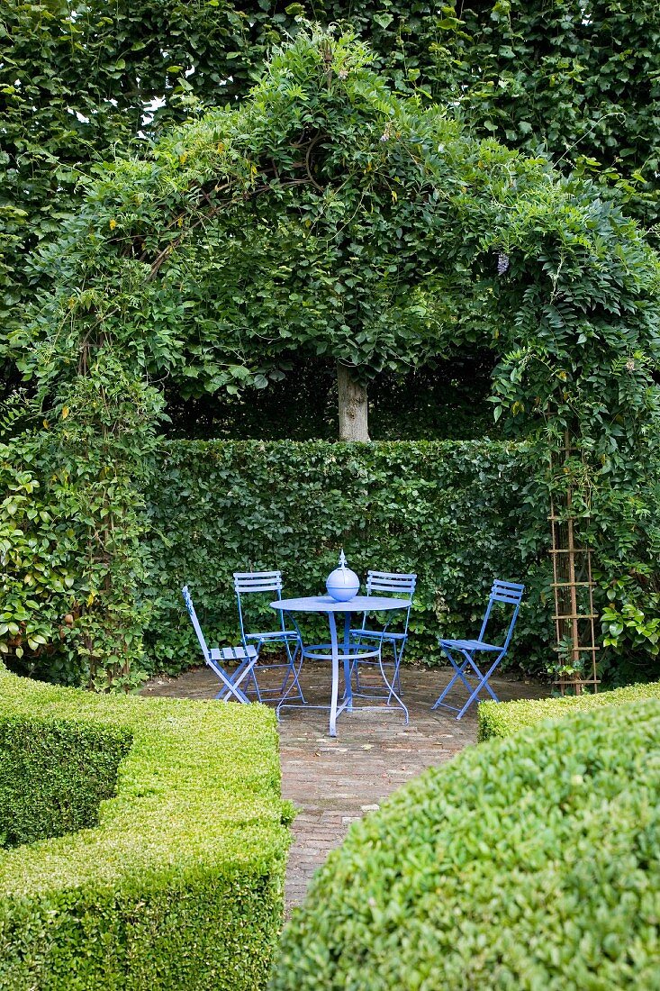 Sitzplatz mit blauen Gartenmöbeln unterm bewachsenen Pavillon