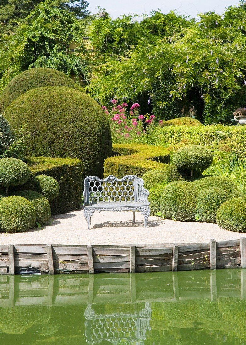Baroque metal bench amongst clipped box hedges next to lake