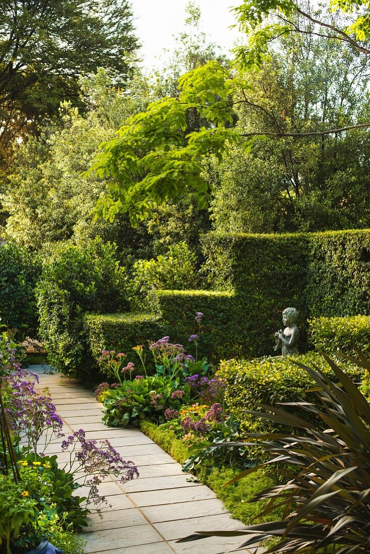 Path leading through summery garden with clipped, stepped hedges