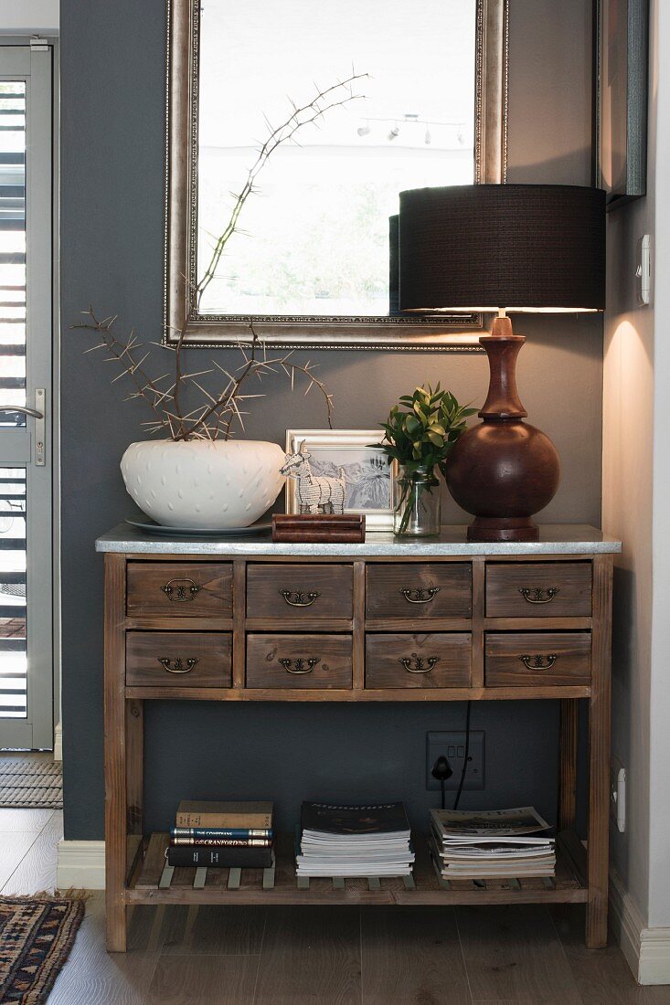 Table lamp on wooden sideboard with drawers against grey wall