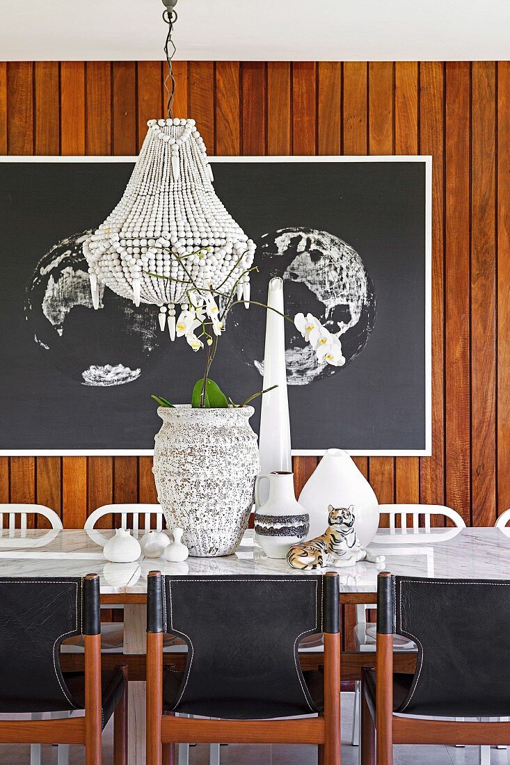 Dining table with marble top and black vintage leather chairs in front of large format picture on wooden wall