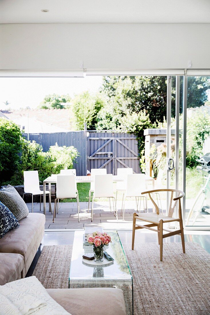 Wohnzimmer mit Fensterfront zum sommerlichen Garten mit Esstisch