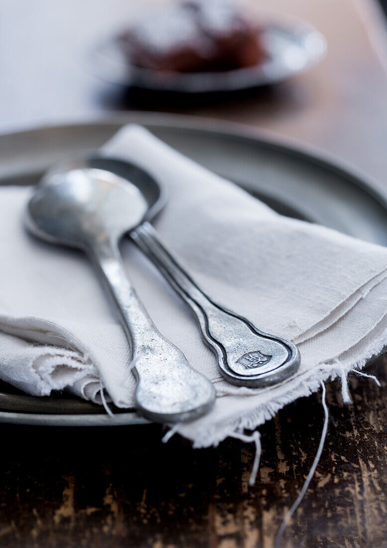 Two old pewter spoons and linen cloth on pewter plate