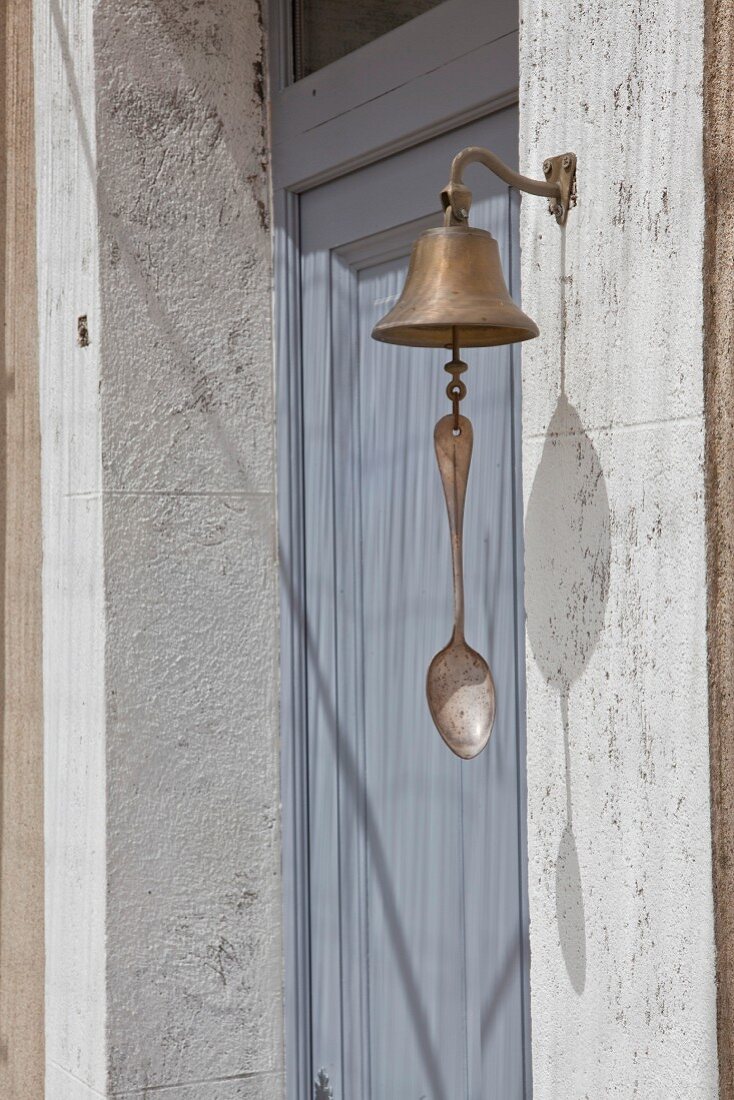 Glockenklöppel mit angebrachtem Vintage Löffel vor graublauer Haustür