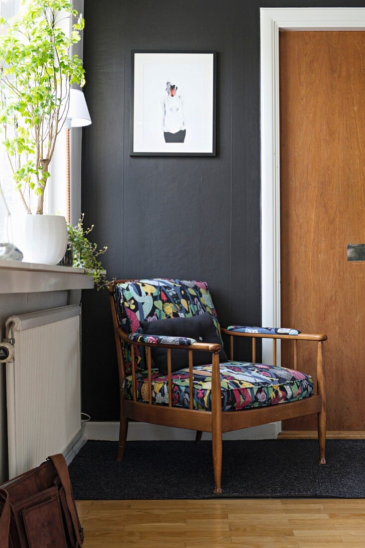 Retro Sessel mit buntem Polsterbezug im Eingangsbereich vor schwarzer Wand mit weißem Türrahmen