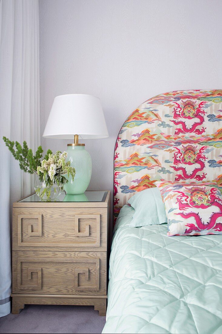 Bedside table with table lamp next to bed with patterned headboard