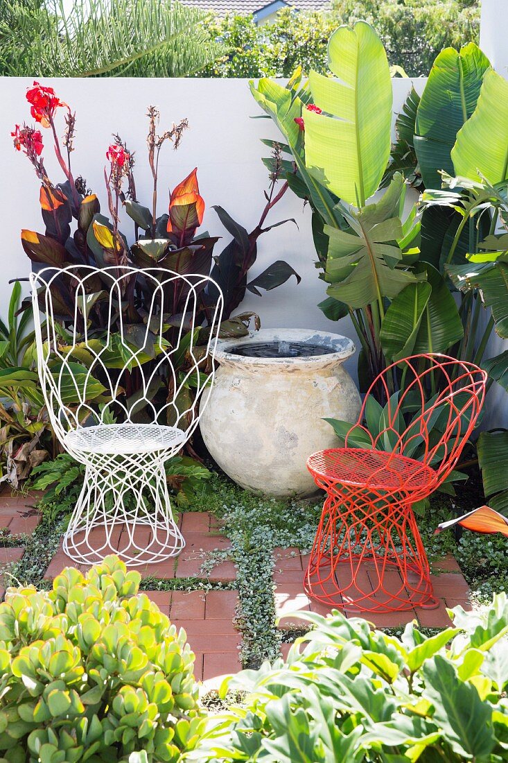 White and red wire armchairs as seating in a green garden corner