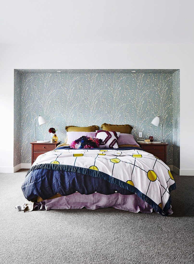 Bett mit verschiedenen Textilien in einer tapazierten Nische