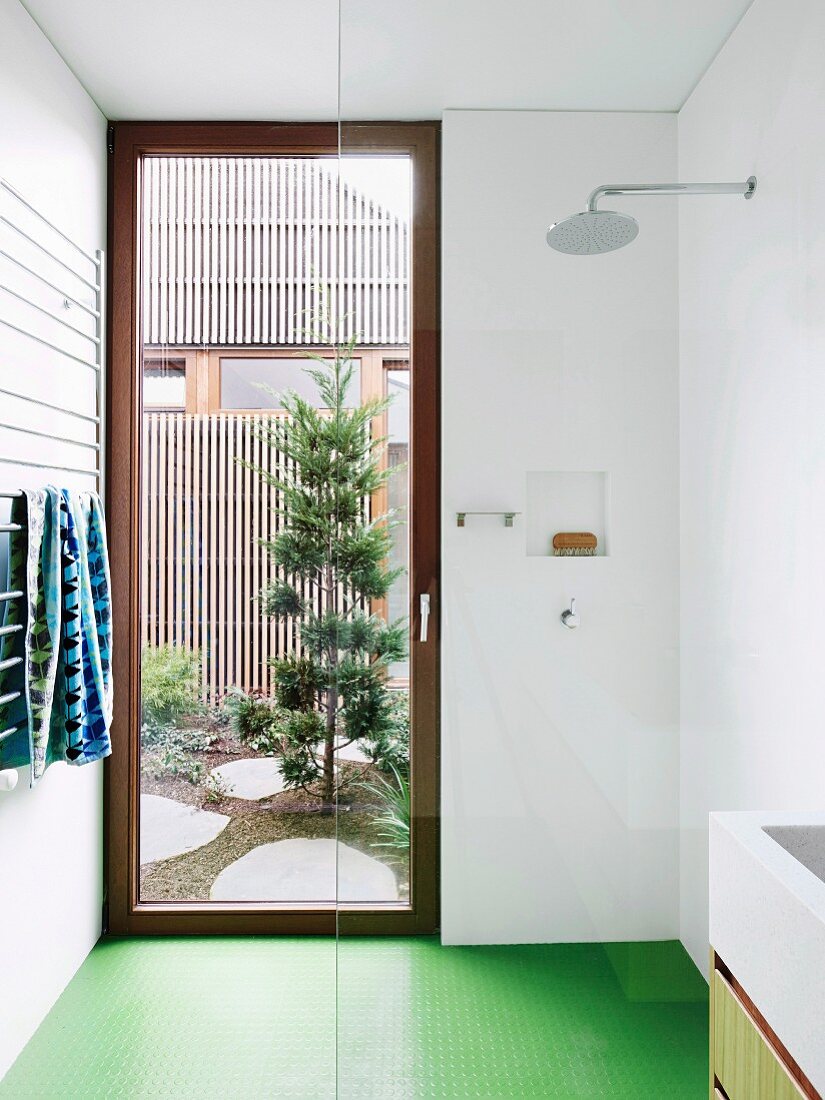 Ebenerdige Dusche mit Glaswand, grünem Boden und Tür zum Hof