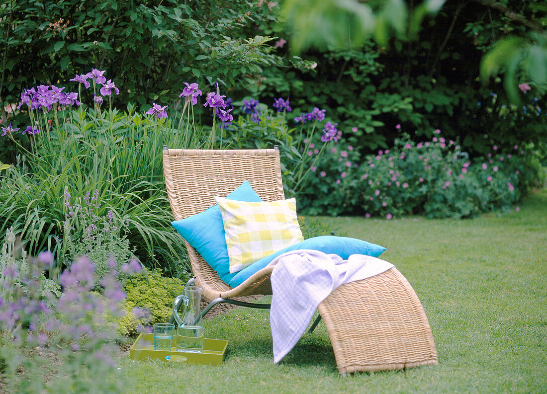 Basket lounger before blue bed with Iris sibirica (meadow iris)
