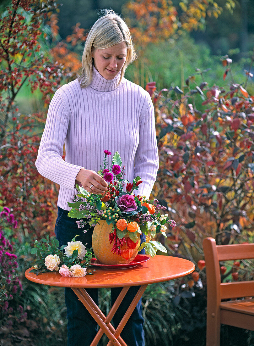 Young woman puts autumn bouquet in cucurbita (pumpkin) as a vase
