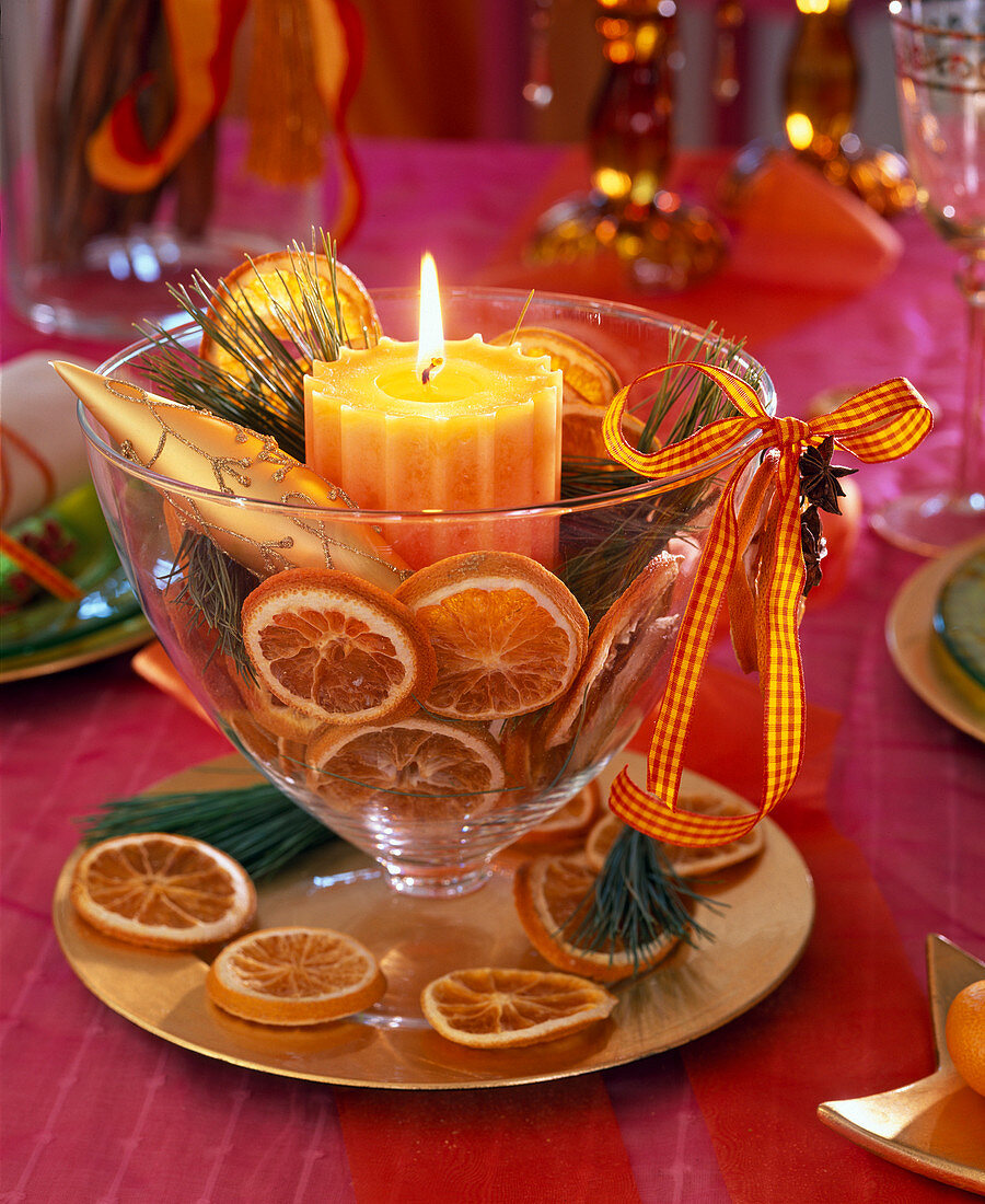 Honigfarbene Kerze im Glaspokal, gefüllt mit Orangenscheiben