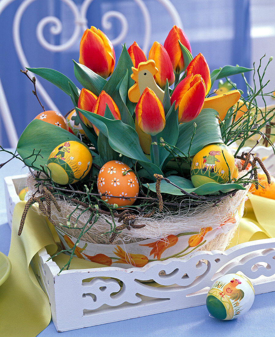 Osternest mit Tulipa (Tulpen), Ostereiern und Hühner-Stecker auf weißem Tablett