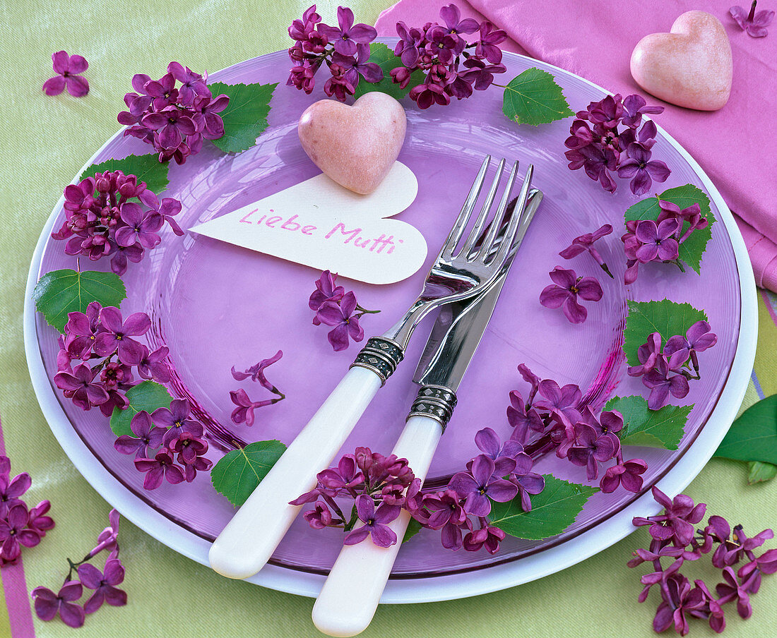 Blüten von Syringa (Flieder) auf lila Glasteller, weißer Platzteller, Herz