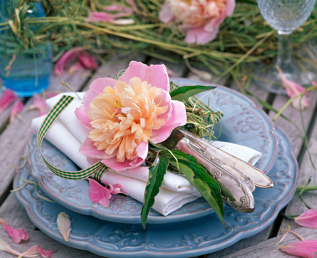 Paeonia blossoms with hay on white cloth napkin, cutlery