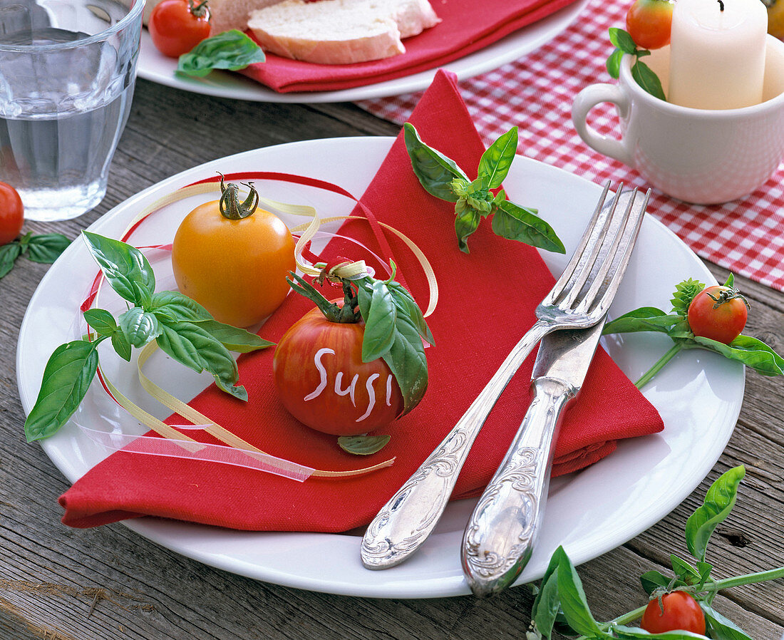 Lycopersicon (Tomate) als Namensschild 'Susi' auf roter Serviette, Ocimum