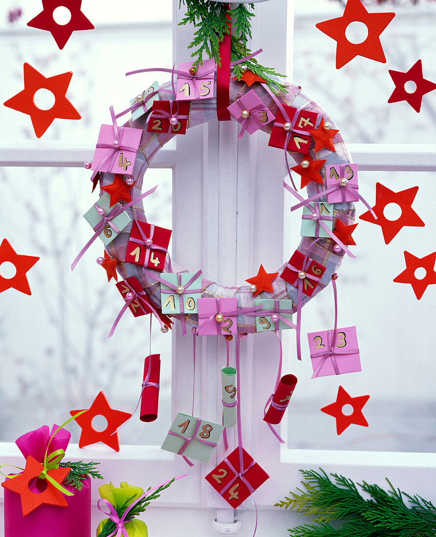 Advent calendar with pastel colored papers hung on a wreath in the window