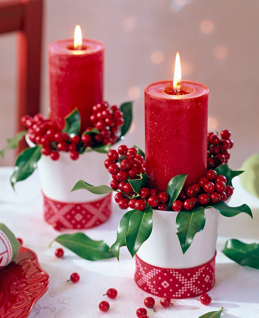 Ilex (Stechpalme) mit roten Kerzen in weißen, mit Band dekorierten Bechern