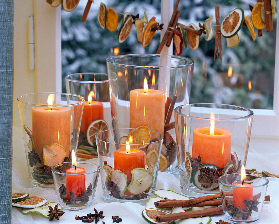Orange Kerzen in Gläsern gefüllt mit getrockneten Scheiben von Malus (Äpfeln)