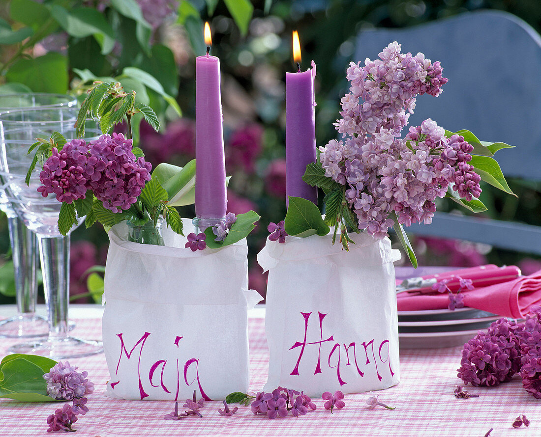 Lila Kerzen in weißen Papiertüten mit Syringa (Flieder), Carpinus (Hainbuche)