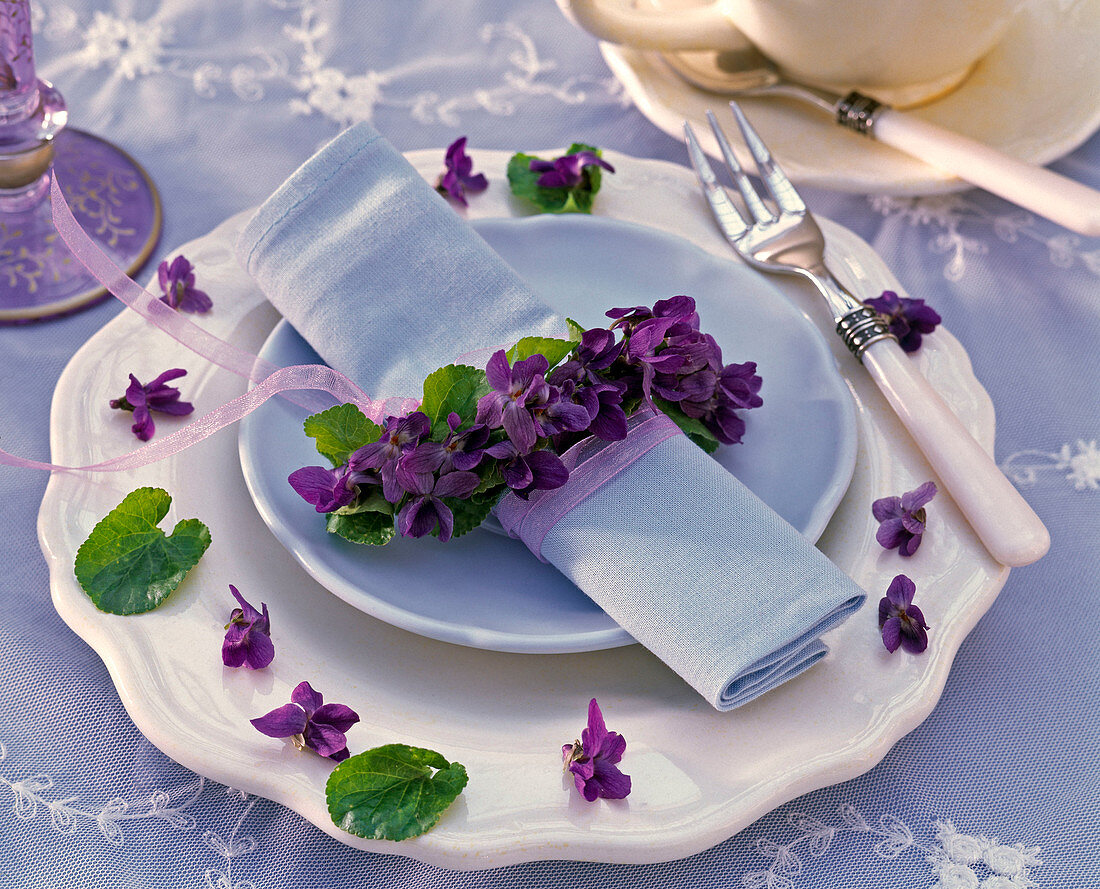 Wreath of Viola odorata around blue napkin, dinner plate, flowers