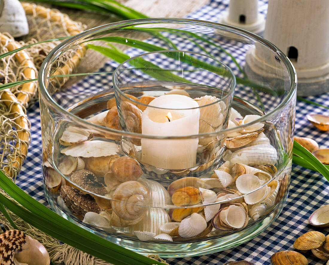 Muscheln in Glasschale mit weißer Kerze auf karierter Tischdecke