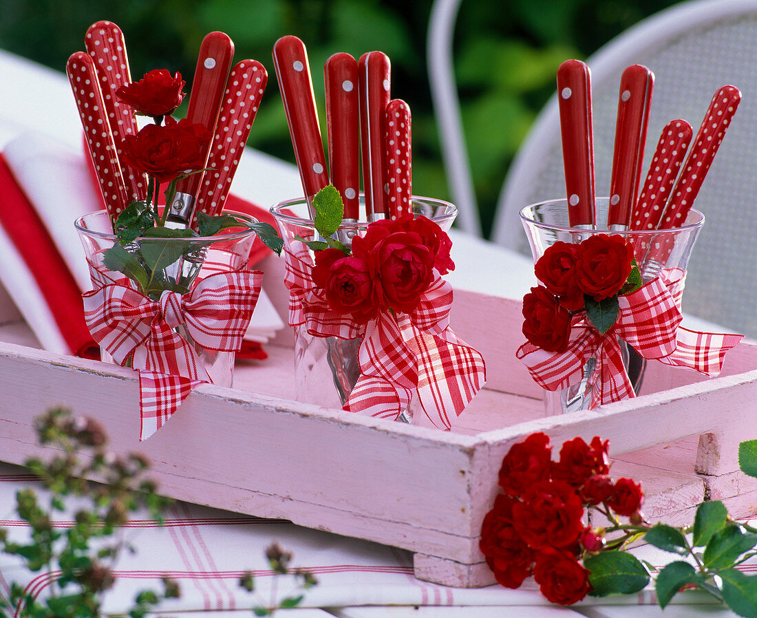 Rosa (Rosen) an Gläsern mit rotem Besteck und Schleifen auf Tablett