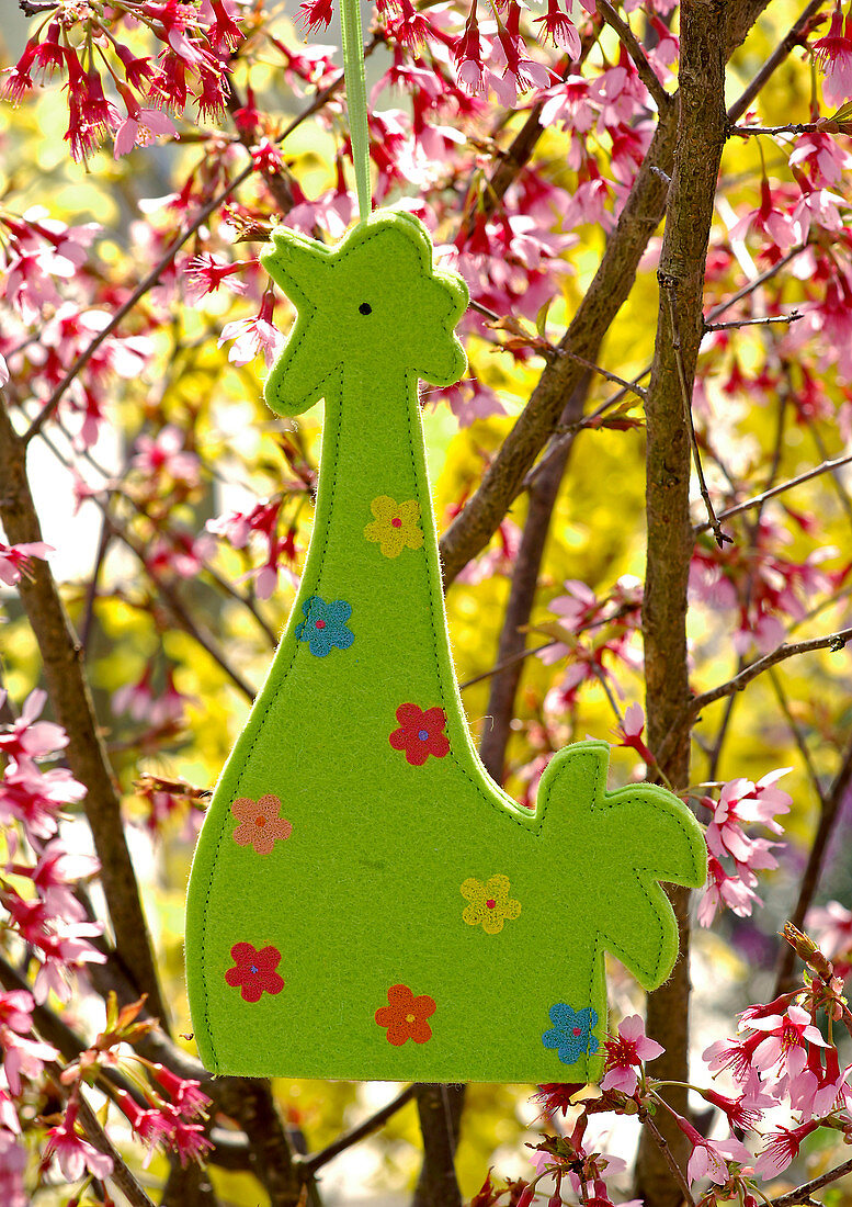 Green felt rooster with flowers hung on Prunus