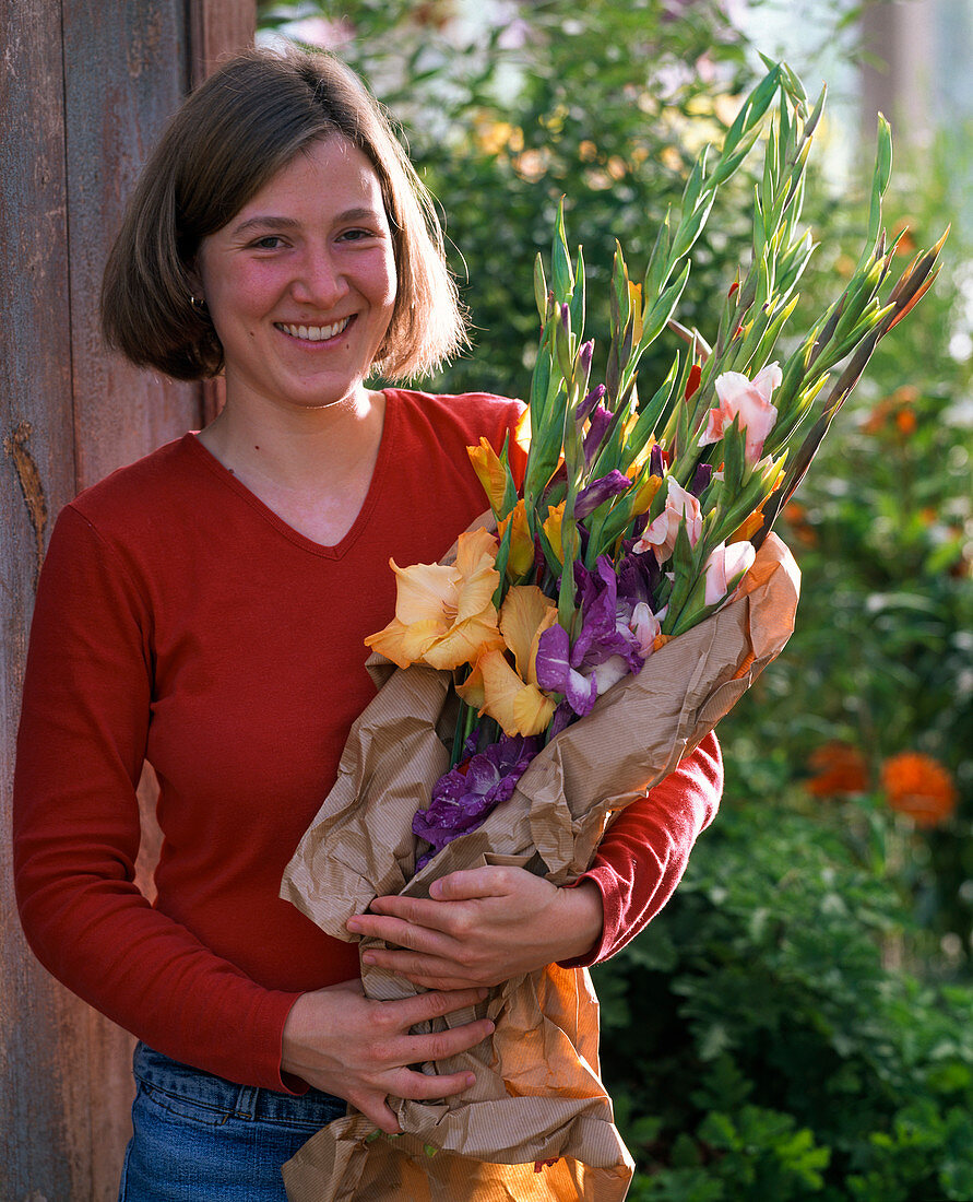 Woman holding a bouquet of gladiolus wrapped in paper in her arms