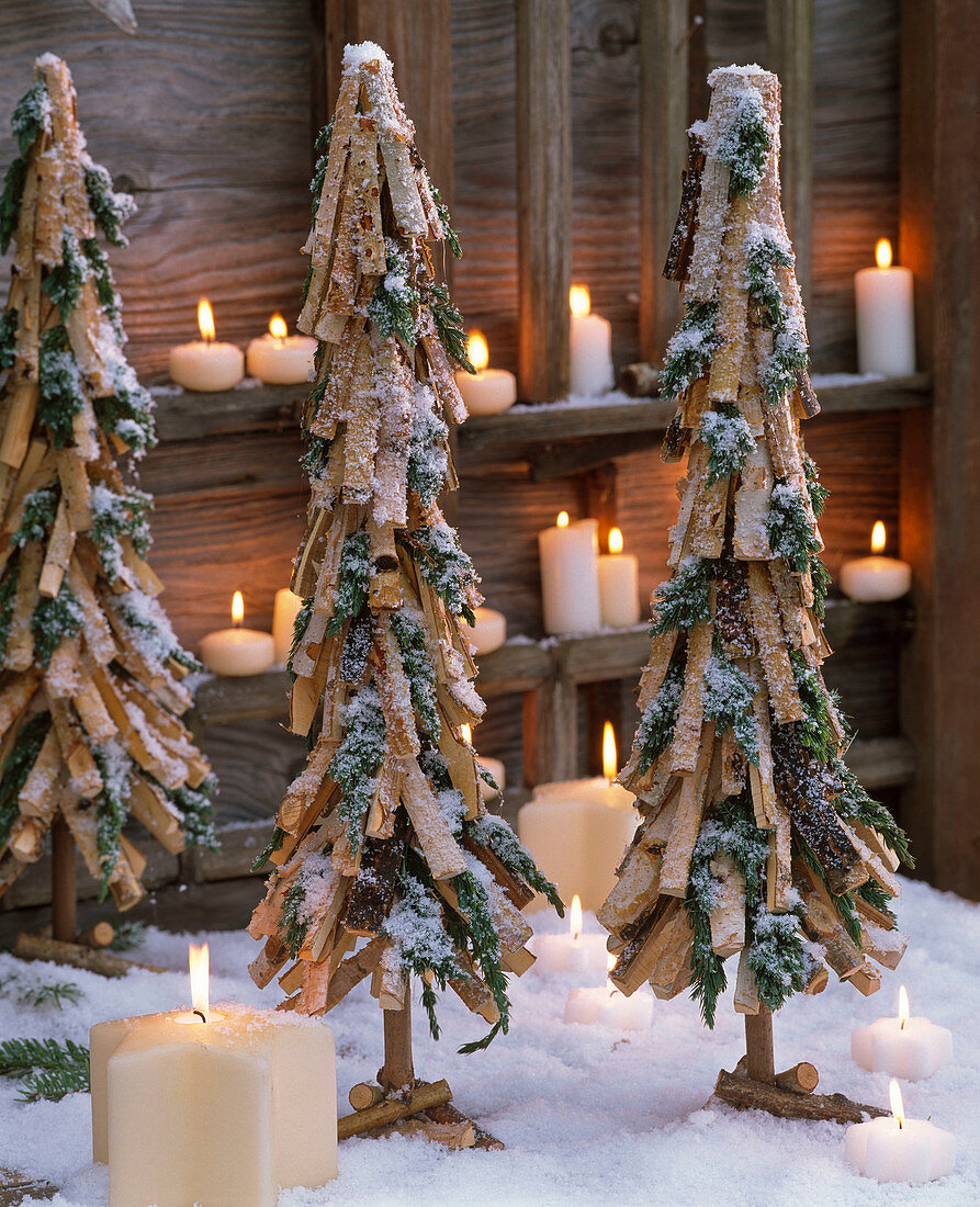 Christmas trees made from Juniperus branches and pieces of wood in the snow, candles