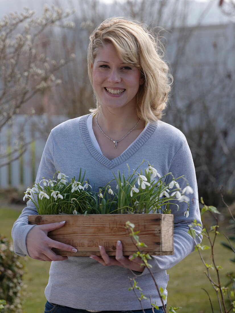 Young woman bringing wooden box with galanthus (snowdrop)
