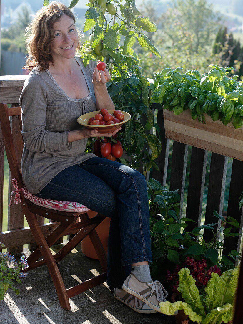 Frau genießt frisch geerntete Tomaten auf dem Balkon