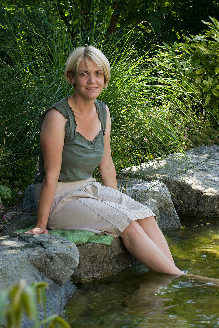 Frau sitzt am Teichrand mit den Füßen im Wasser