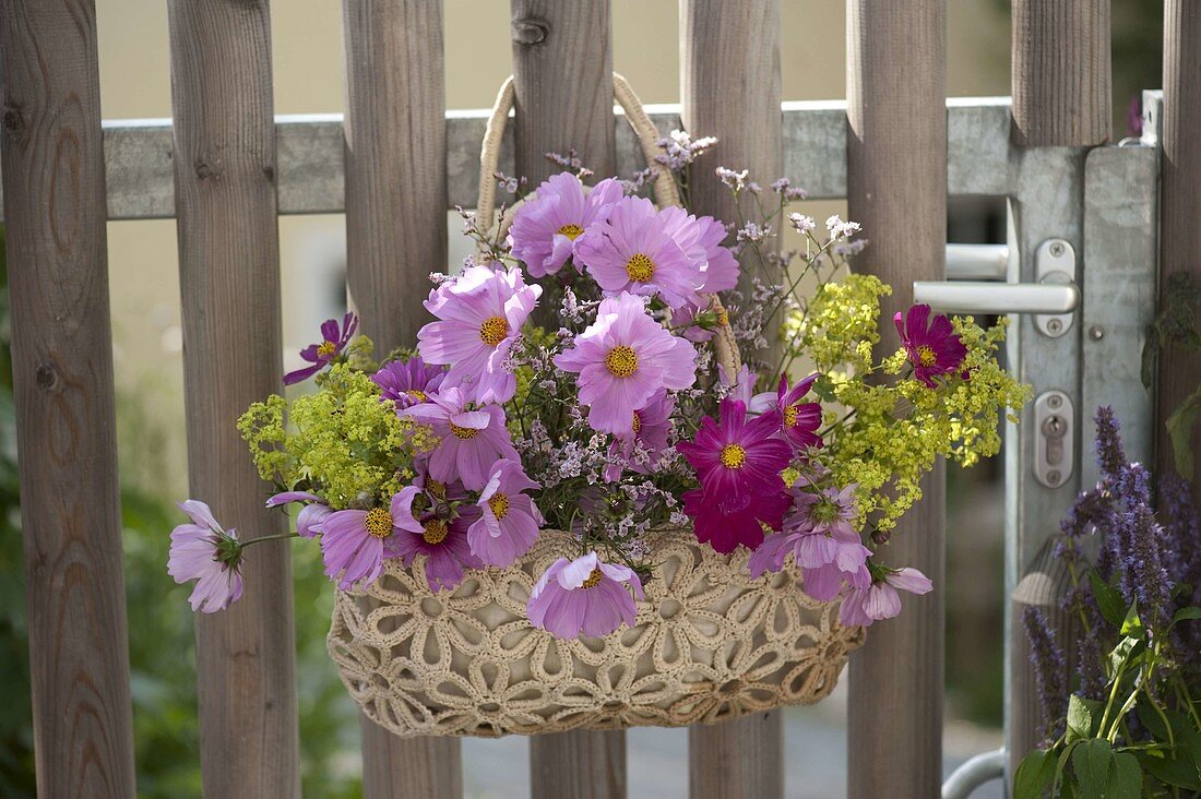 Tasche mit Sommerblumen als Willkommensgruß an Gartentor gehängt