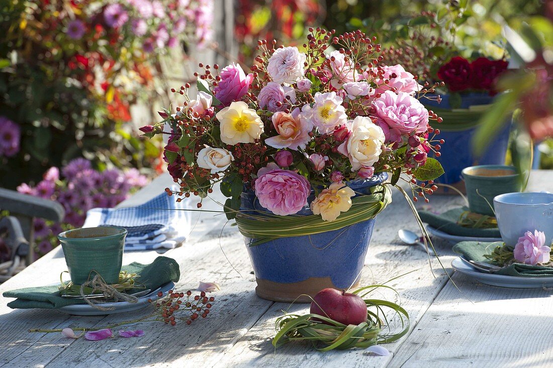 Herbstlicher Strauß aus Rosa (Rosen) und Hagebutten in blauer Vase