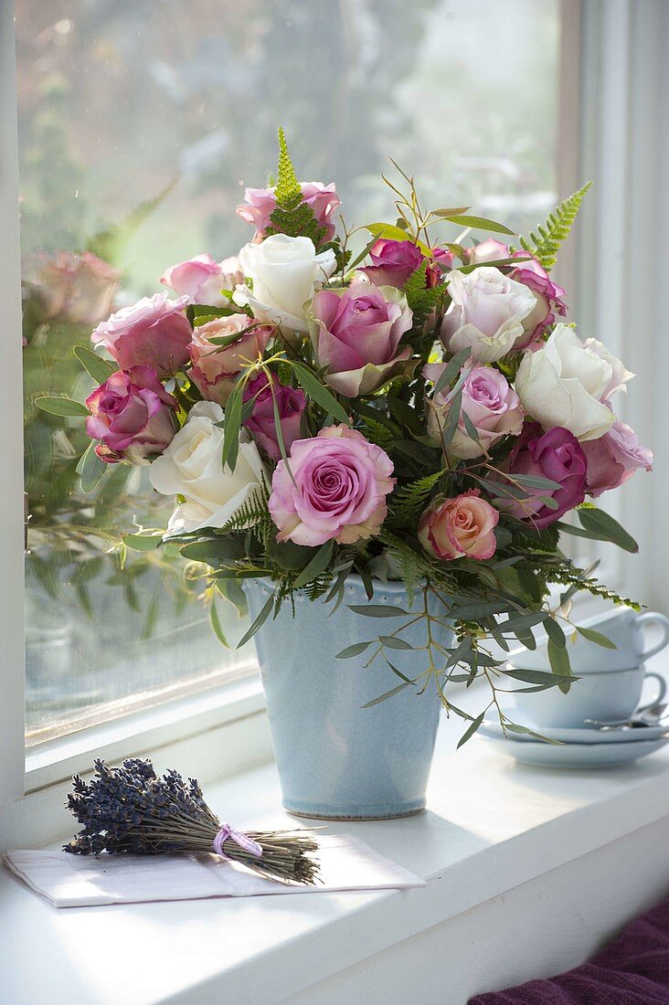 Strauß aus Rosa (Rosen), Eukalyptus und Farn in blauer Vase am Fenster