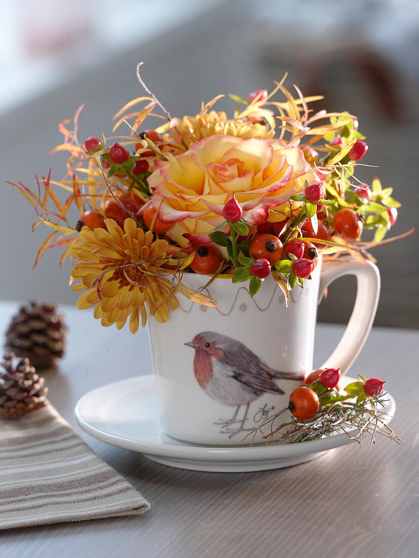 Cup with robin decoration filled with roses and rosehips