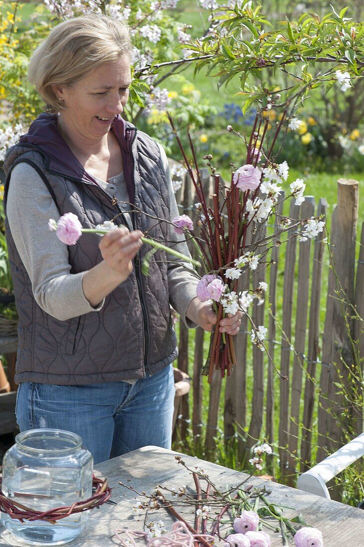 Frau bindet Steh-Strauss mit Zweigen von Cornus (Hartriegel), Prunus