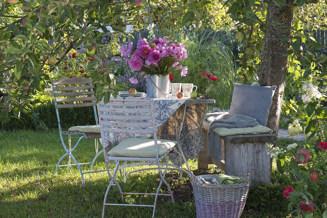 Table laid under apple tree with bouquet of summer flowers