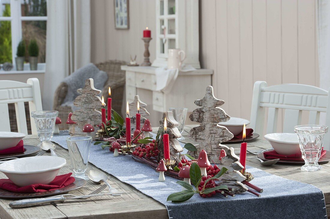 Table laid with small Christmas trees made of birch bark, red berries