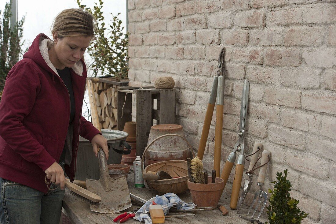 Frau säubert Spaten mit einer Bürste, saubere Werkzeuge lehnen